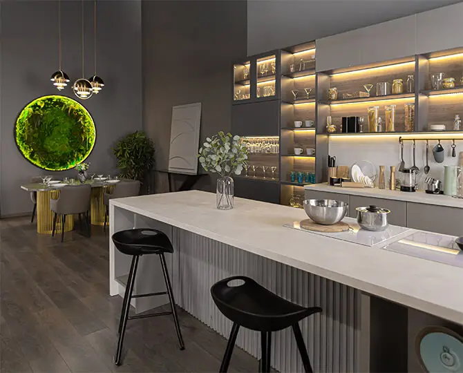 Modern kitchen with a white island, black stools, and illuminated shelves displaying glassware.
