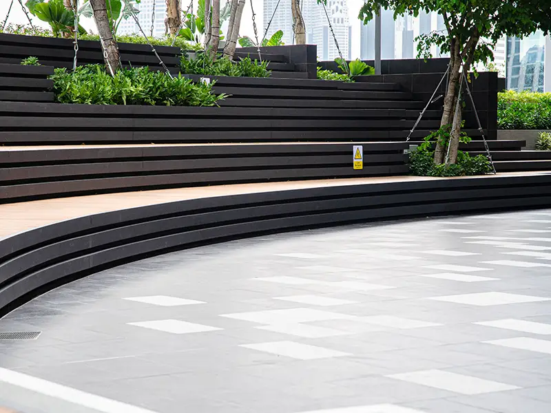 Curved black seating steps surrounded by greenery and trees in an outdoor amphitheater.