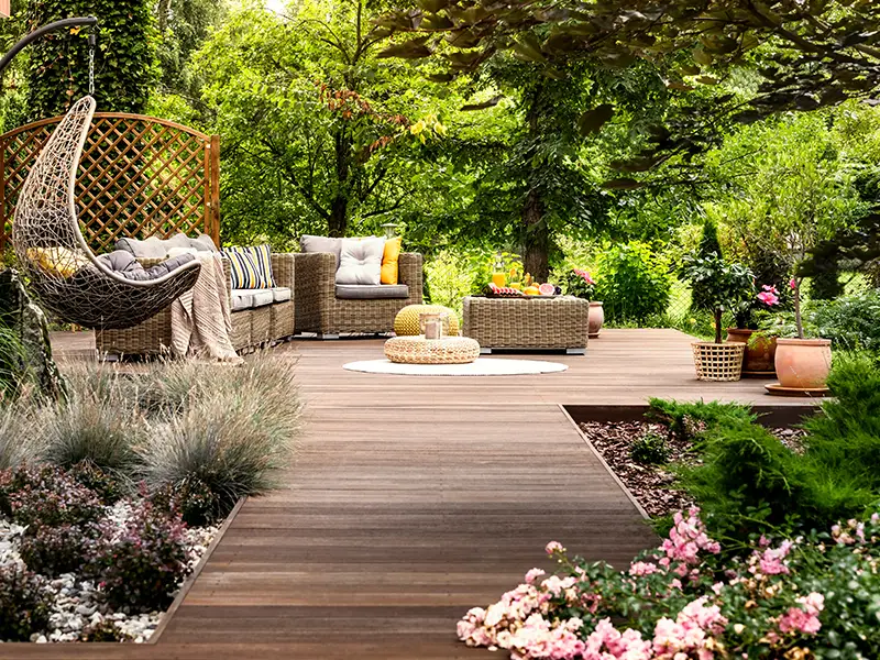 A cozy outdoor seating area with a hanging chair, wicker furniture, and colorful flowers.