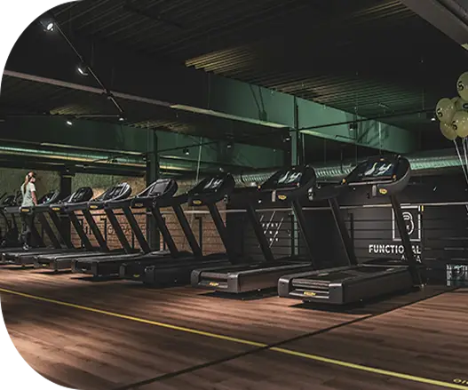 Row of treadmills in a modern gym with wooden flooring and mirrors.