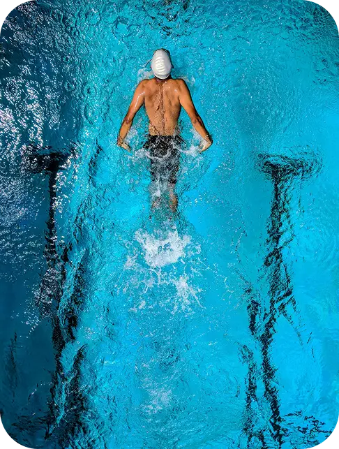 A swimmer in a white cap glides through bright blue water, creating splashes.