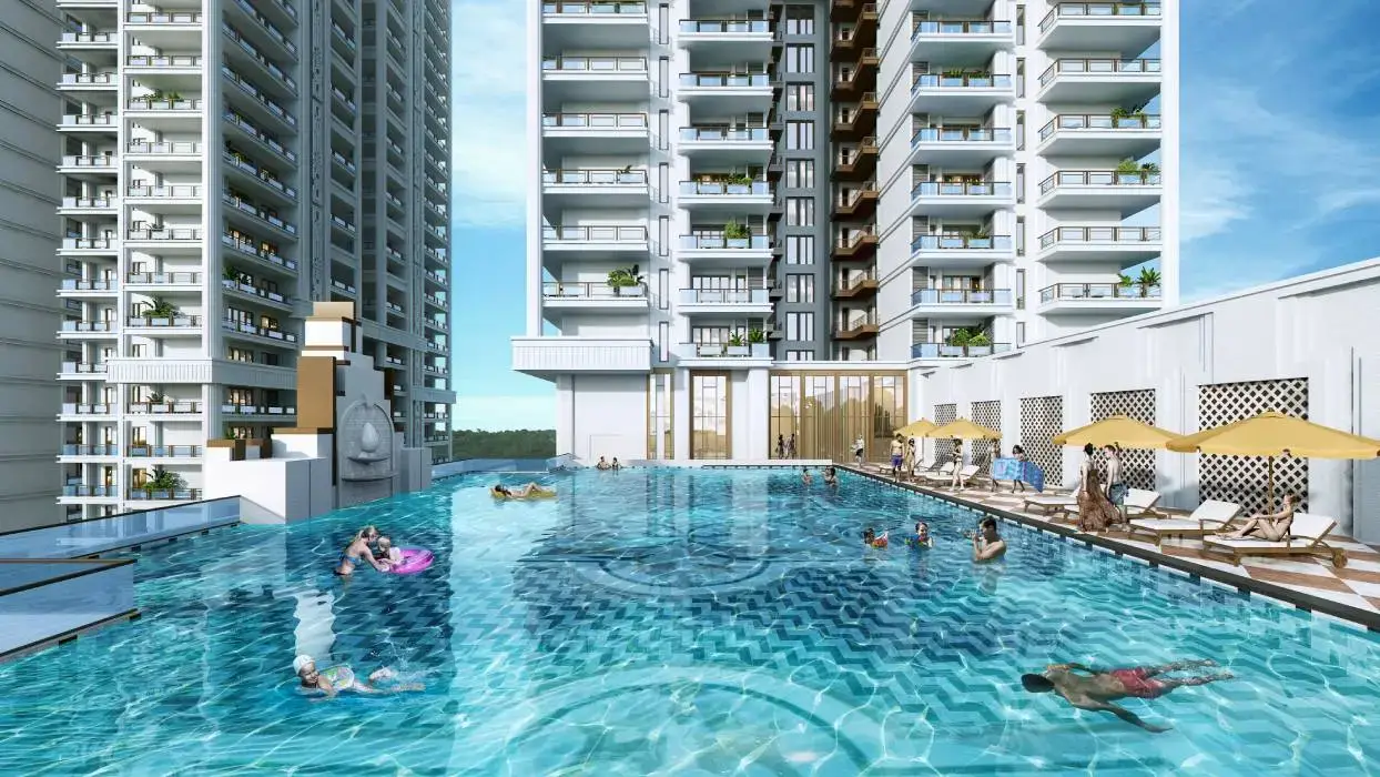 A large swimming pool surrounded by modern buildings, with people swimming and lounging on deck chairs.