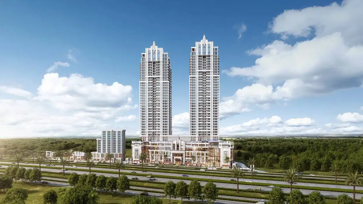 Two tall residential towers with a modern design, surrounded by greenery and a clear blue sky.