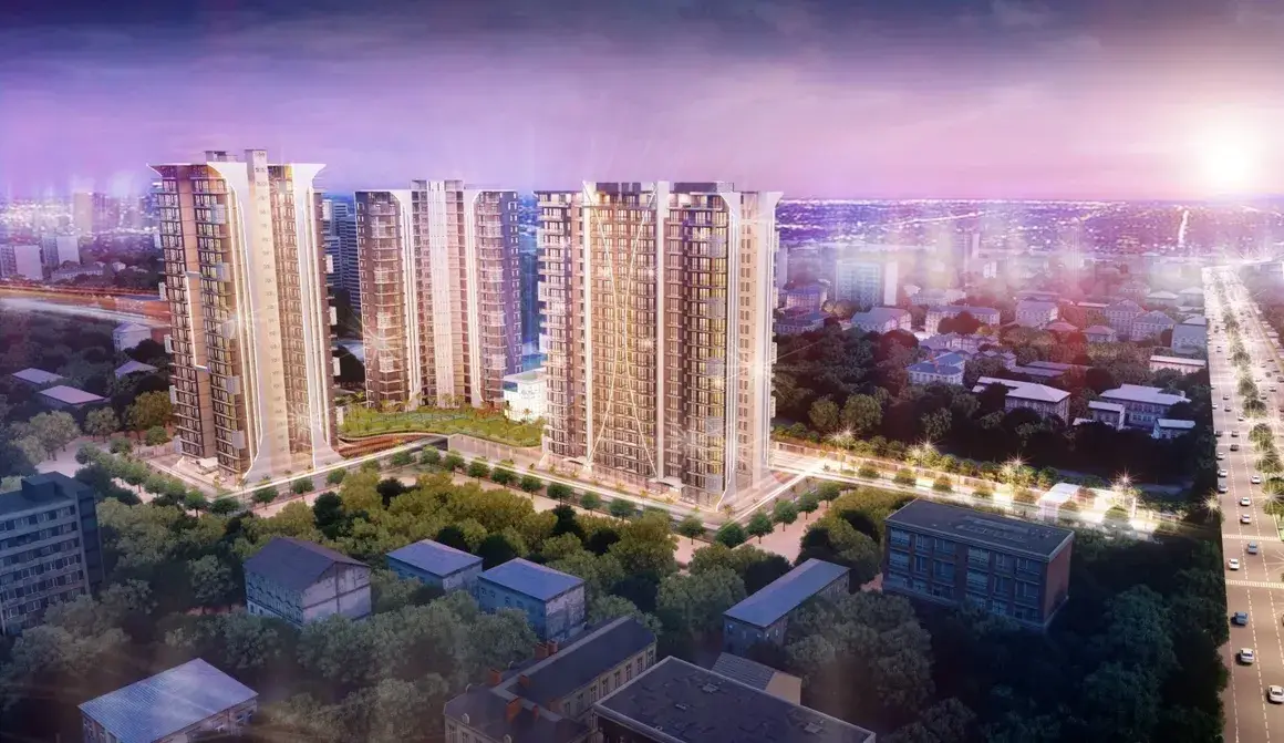 Aerial view of three tall residential buildings surrounded by greenery and urban landscape at sunset.