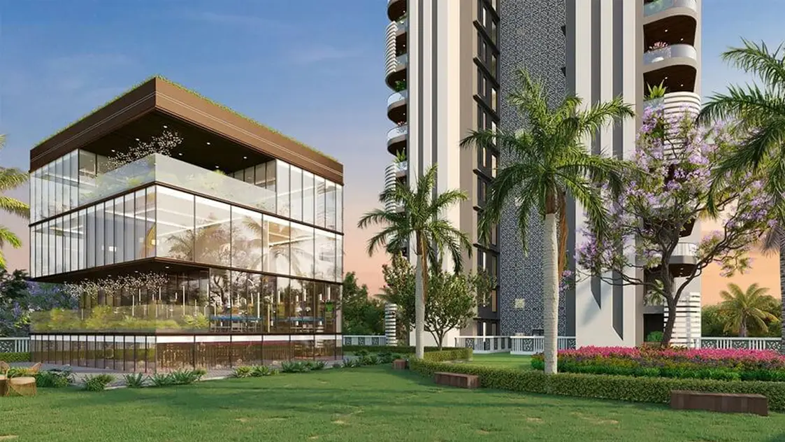 A glass building surrounded by greenery and palm trees, next to a tall residential structure.