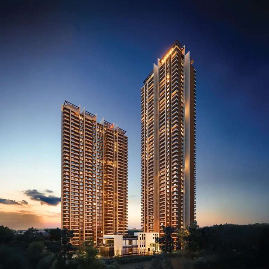 Two tall residential towers illuminated at dusk with a landscaped area in the foreground.