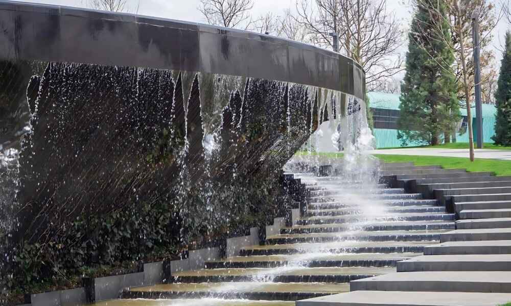 A modern water feature with cascading water over a curved black surface and stone steps.