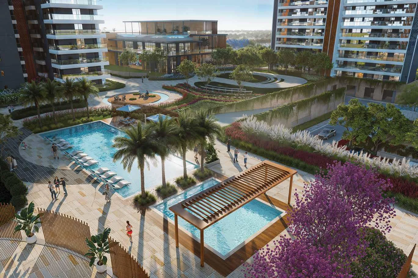 Aerial view of a landscaped area with pools, palm trees, and modern buildings in the background.