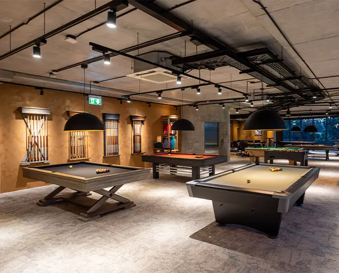 Interior view of a games lounge with multiple pool tables and modern lighting.