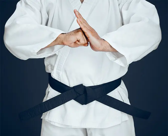Person in a white karate uniform with a black belt, hands positioned in a defensive stance.