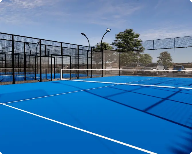 Blue tennis court with netting, surrounded by trees and parking area, under clear sky.