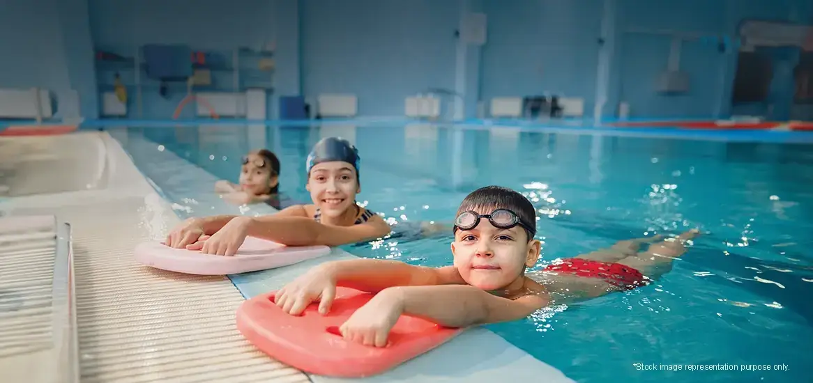 Three children swimming in a pool with flotation devices, smiling and enjoying the water.