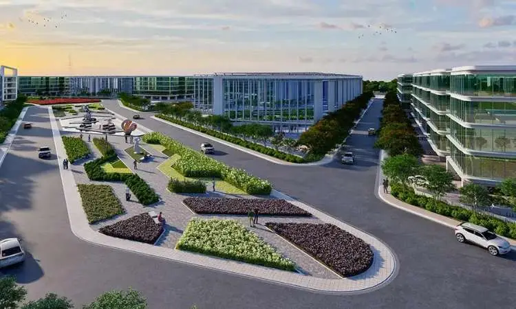 A landscaped area with curved pathways, greenery, and modern buildings along a wide road.