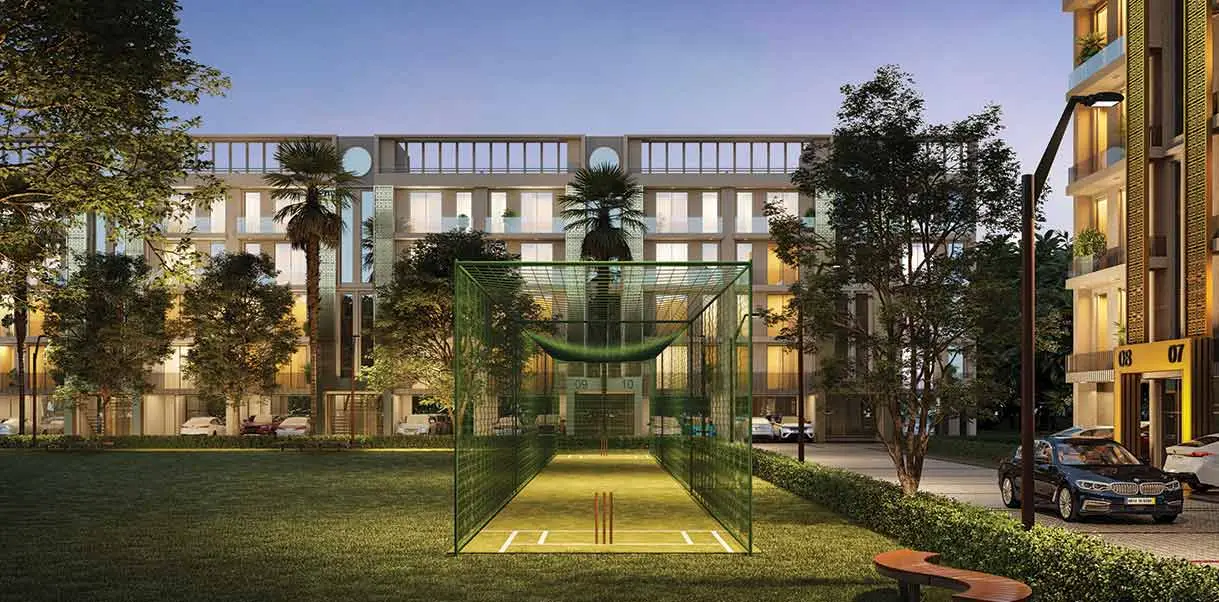 A cricket practice net surrounded by trees and modern buildings at dusk.
