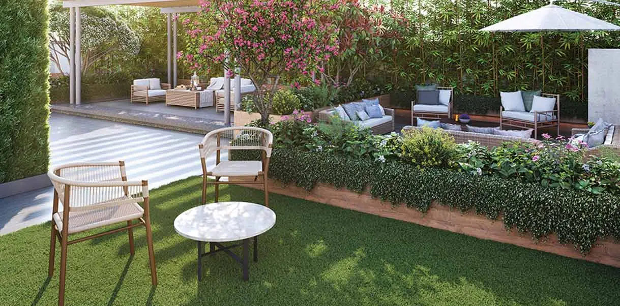 A landscaped garden with chairs, a small table, and lush greenery, featuring a shaded area.