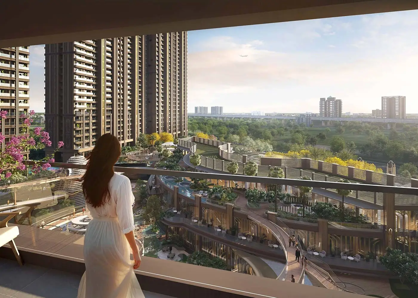 A woman in a white dress stands on a balcony overlooking a landscaped area and buildings.