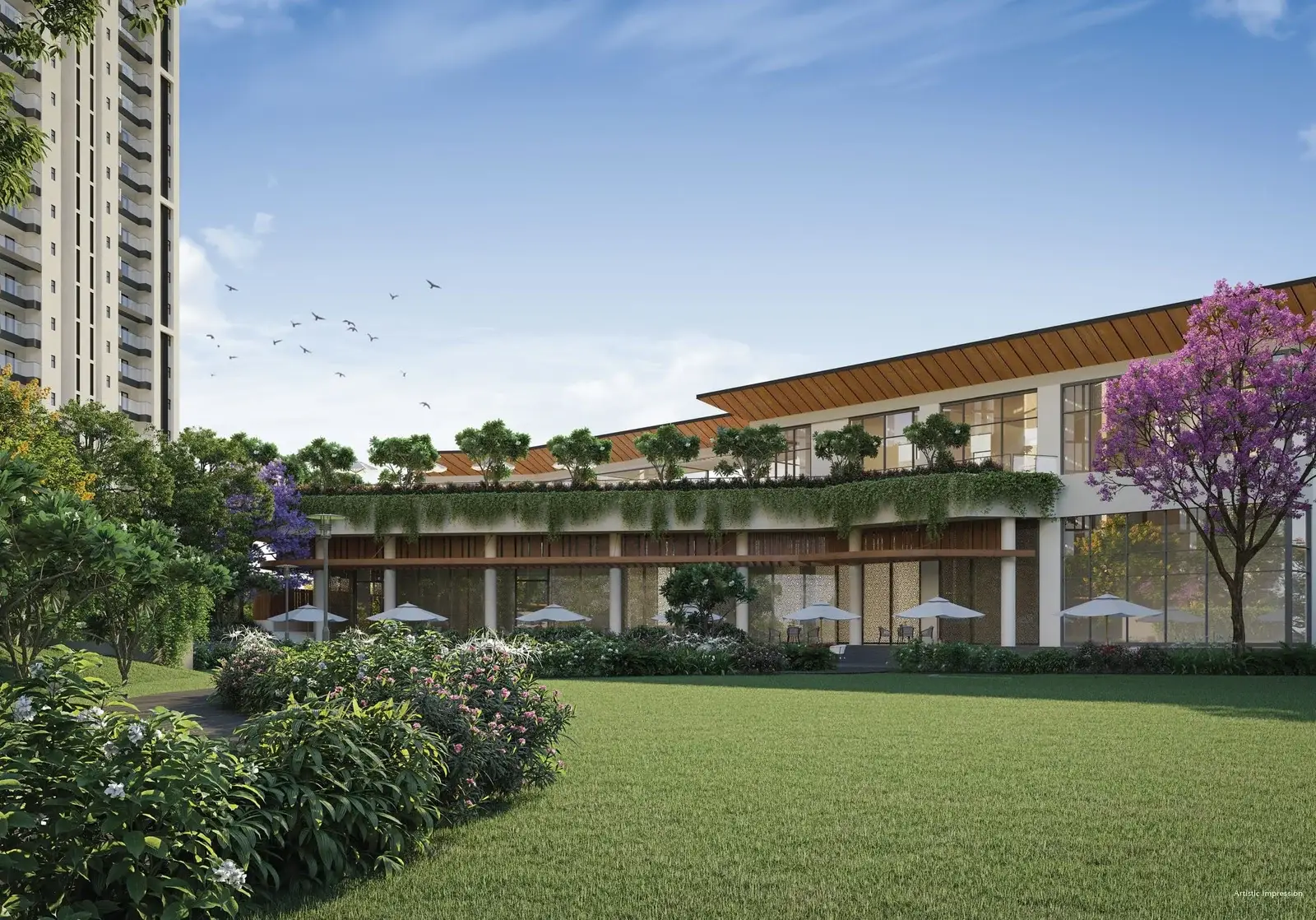 Modern building with large windows surrounded by greenery and purple flowering trees under a clear blue sky.