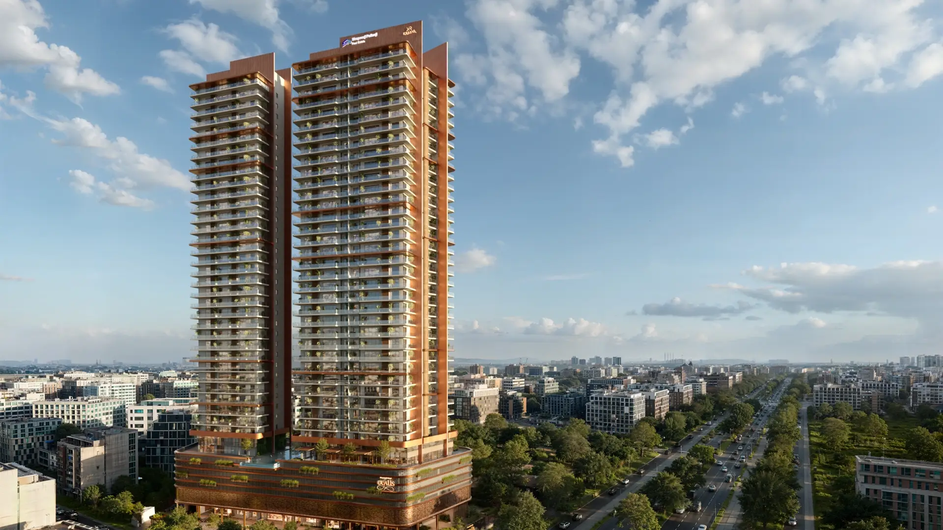 Two tall residential towers with balconies, surrounded by greenery and cityscape under a cloudy sky.