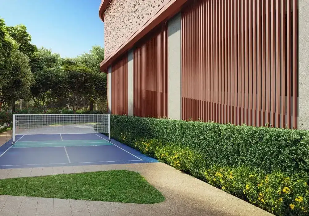 A blue tennis court with a net, surrounded by green hedges and a modern building.