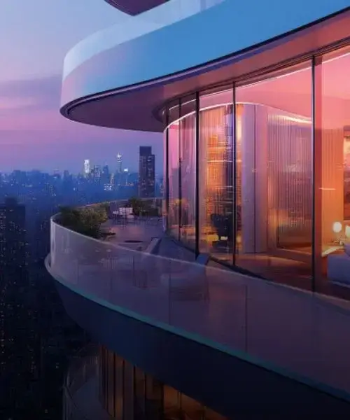Curved balcony with glass railing overlooking a city skyline at dusk with warm lighting.