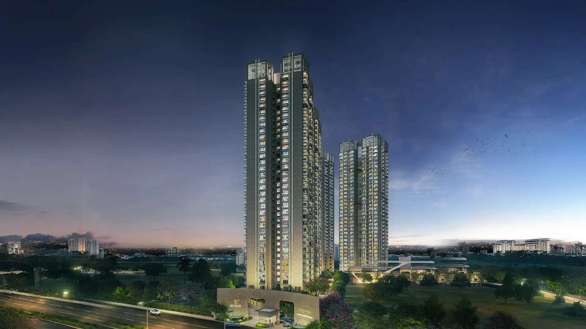 Three tall residential buildings at dusk, surrounded by greenery and a road in the foreground.
