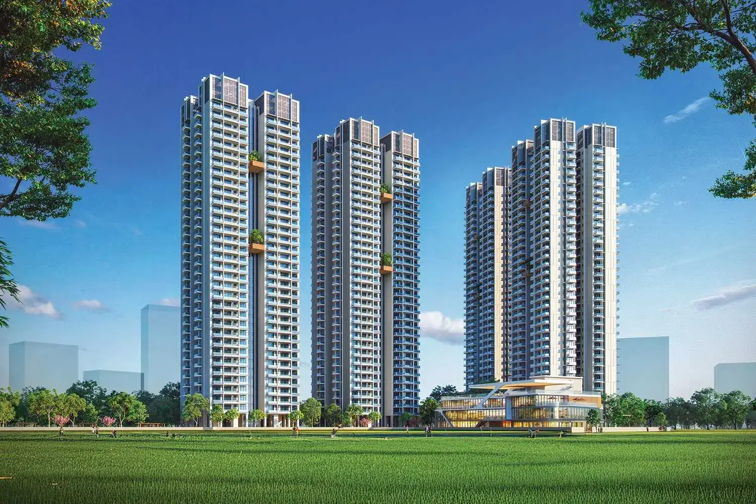 Four tall residential towers with balconies and a modern building in front, surrounded by green grass.