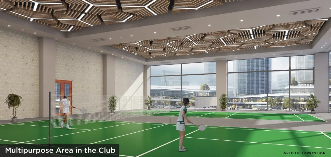 Indoor multipurpose area with green flooring, large windows, and two individuals playing badminton.