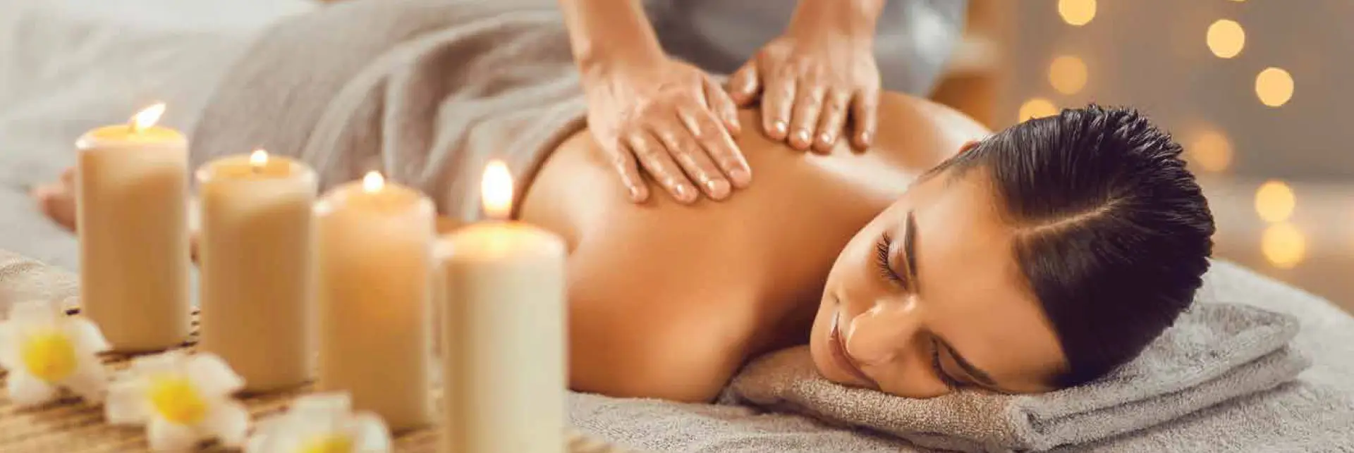 A woman receiving a massage with candles and flowers in the foreground, creating a relaxing atmosphere.