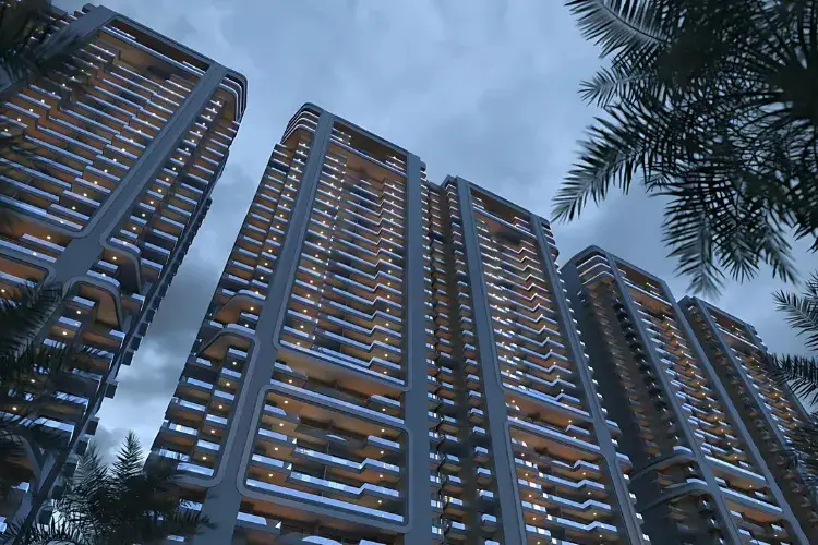 Tall residential towers illuminated at night with a cloudy sky and palm trees in the foreground.