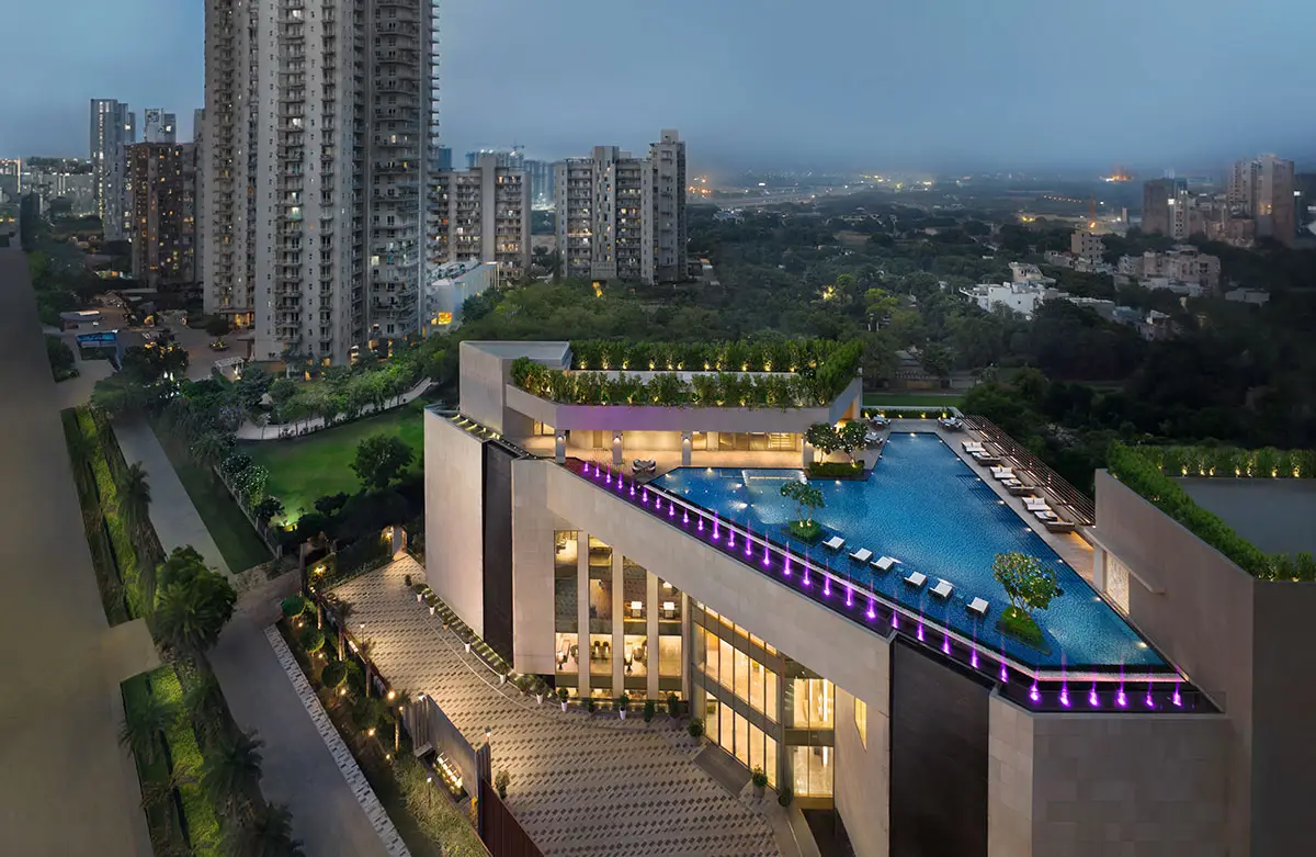 Aerial view of a contemporary building with a rooftop pool and surrounding greenery at dusk.