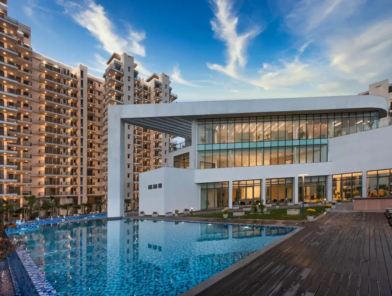 Contemporary building with large glass windows beside a swimming pool and high-rise apartments.