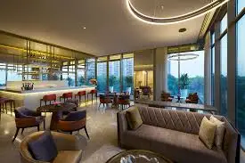 Modern lounge with large windows, plush seating, and a bar area in the background.