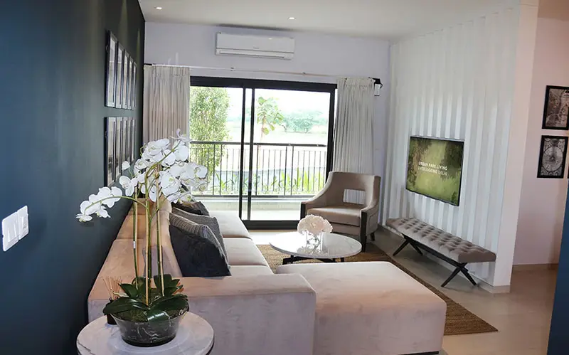 Modern living room with a beige sofa, glass table, and large window overlooking greenery.