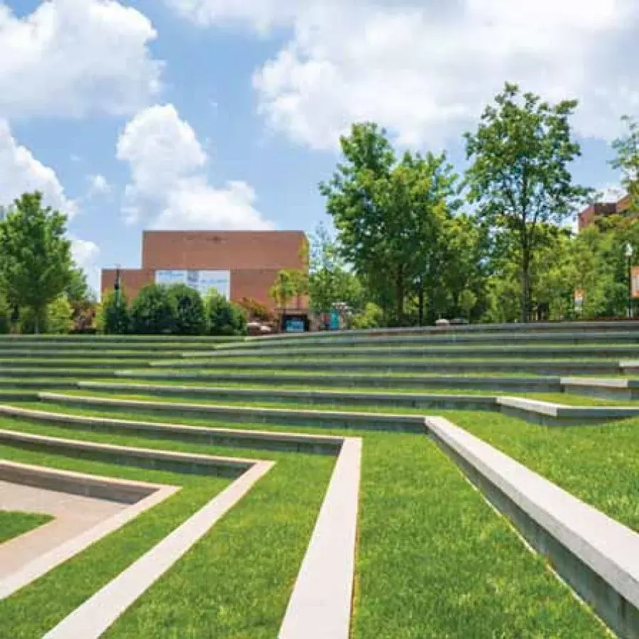 Green amphitheatre with tiered seating and surrounding trees under a blue sky.