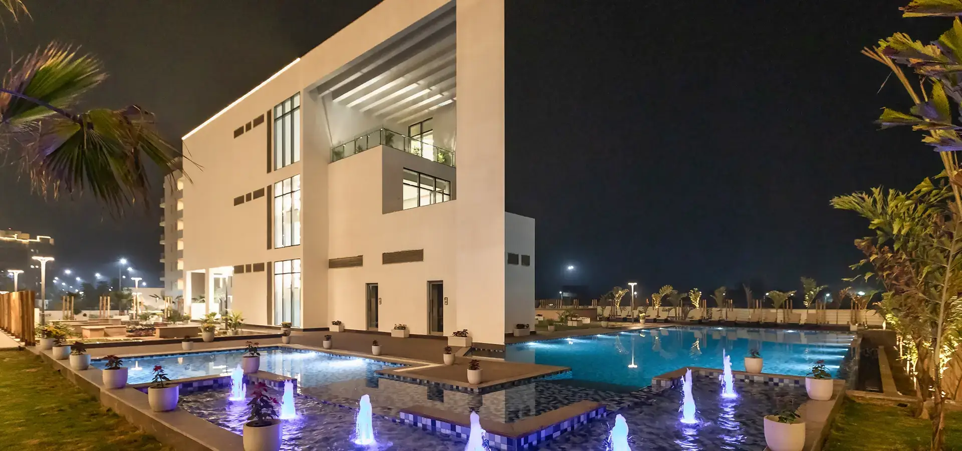 Contemporary building at night with illuminated water features and landscaped surroundings.