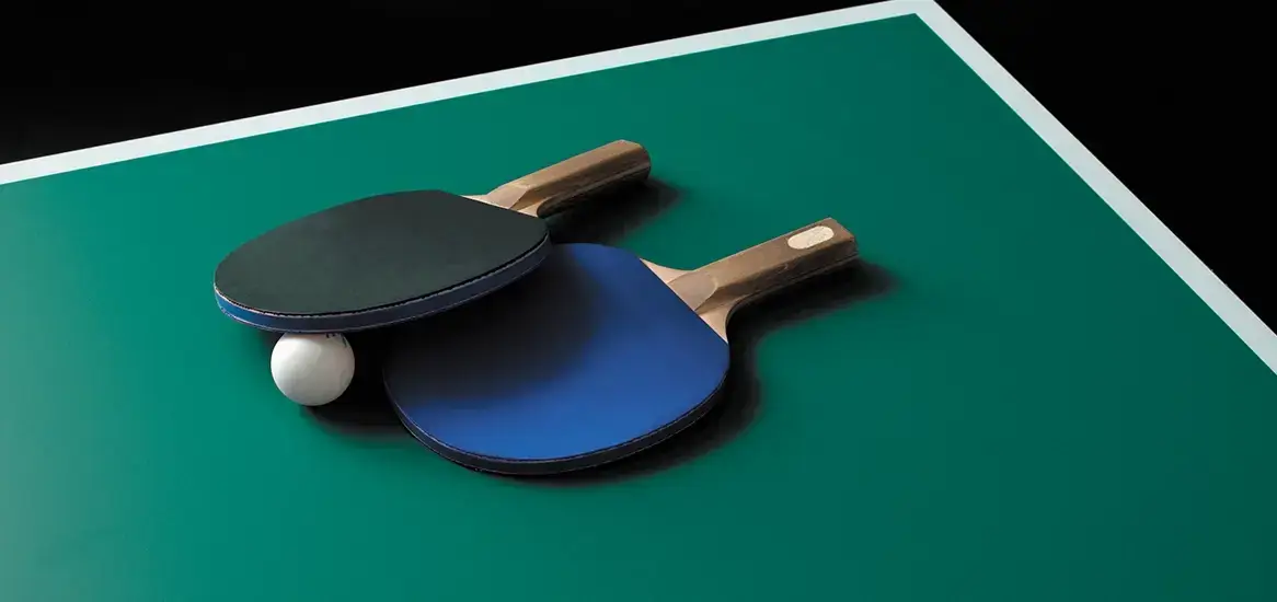 Two table tennis paddles in black and blue resting on a green table with a white ball.