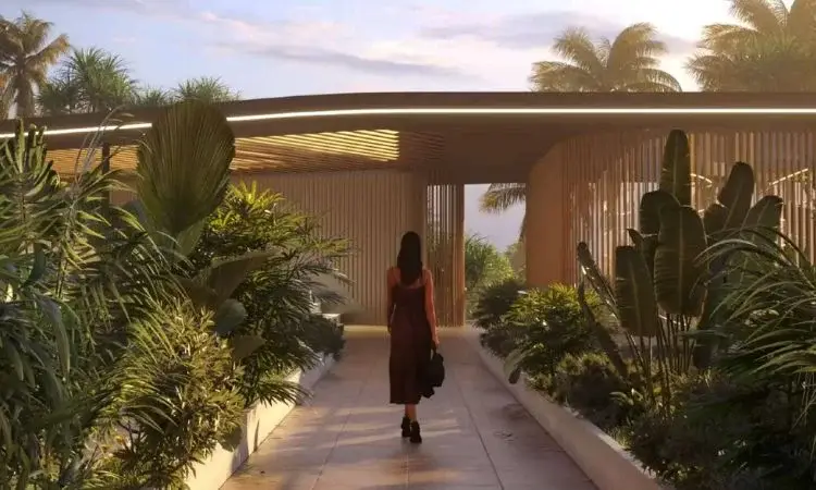 A woman walks along a pathway surrounded by lush greenery and modern architecture.