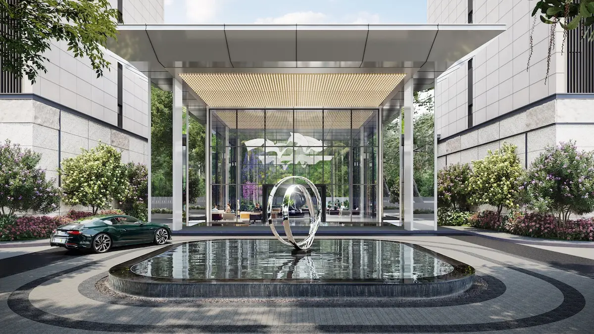 Modern building entrance with a water feature, sculpture, and landscaped greenery.