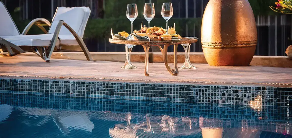 A wooden table with snacks and drinks beside a swimming pool and lounge chairs.