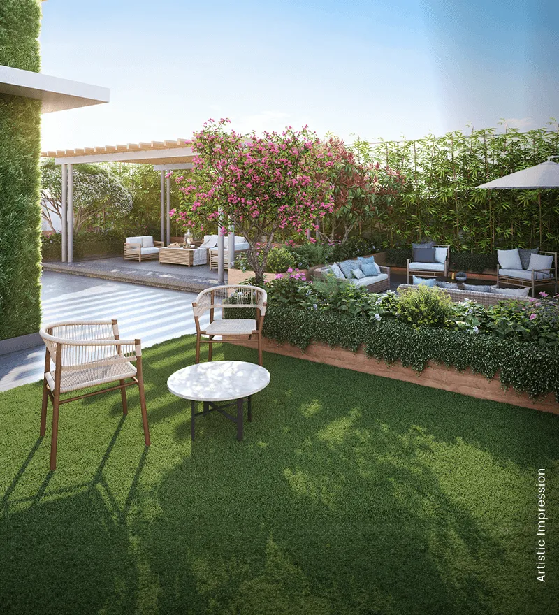 A landscaped garden with green grass, chairs, a table, and flowering plants in the background.