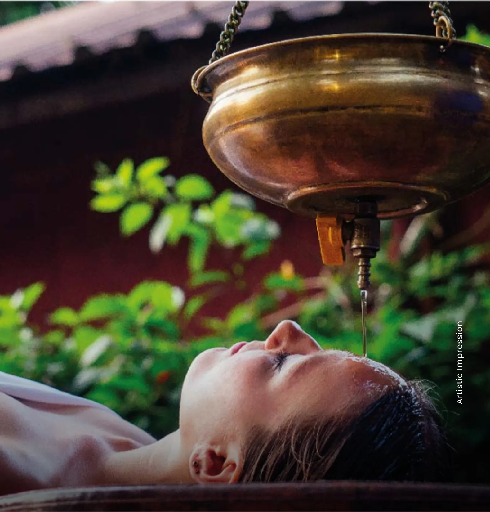A woman receiving an Ayurvedic treatment with oil dripping from a brass vessel onto her forehead.