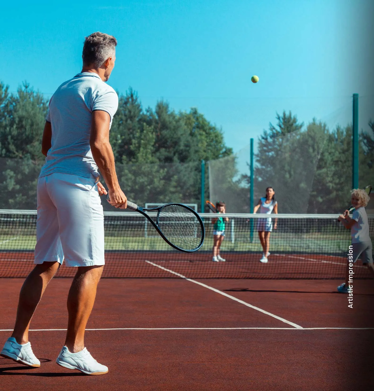 A man in white prepares to hit a tennis ball while children play in the background.