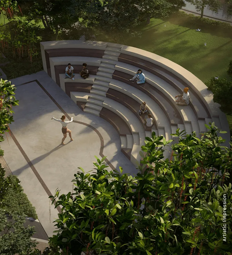 An open amphitheater with people seated, surrounded by greenery and a dancer performing.