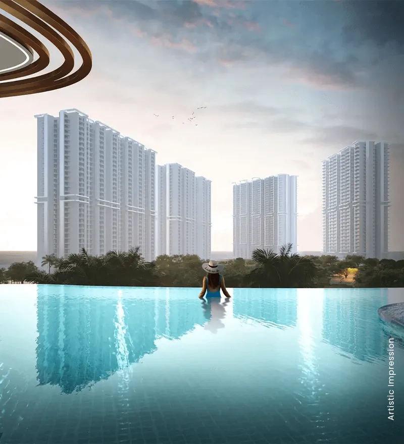A person in a hat sits at the edge of an infinity pool, overlooking tall residential buildings.