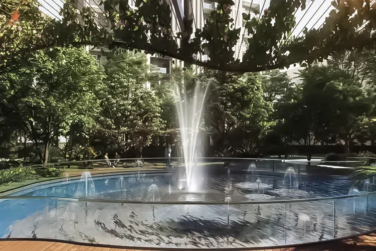A circular water fountain surrounded by lush greenery and trees in a landscaped area.