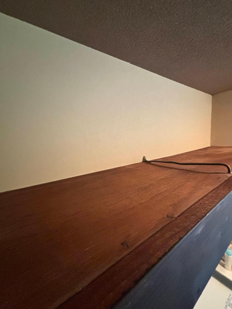Close-up view of a wooden shelf with a power cord on top, against a neutral-coloured wall.