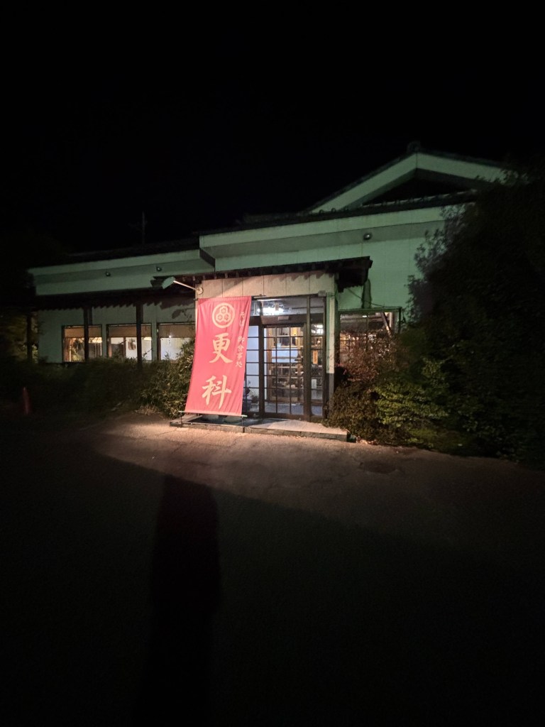 Front view of a restaurant at night featuring a large red banner with Japanese characters.