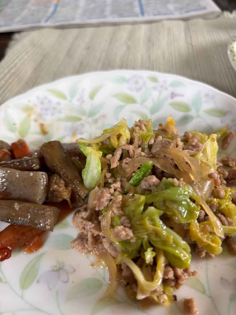 A plate of food featuring minced meat mixed with chopped green vegetables and served alongside sliced pickled vegetables.