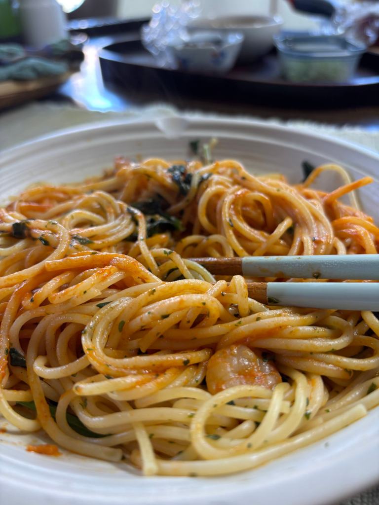 Close-up of a bowl of spaghetti with shrimp and herbs, served with chopsticks.