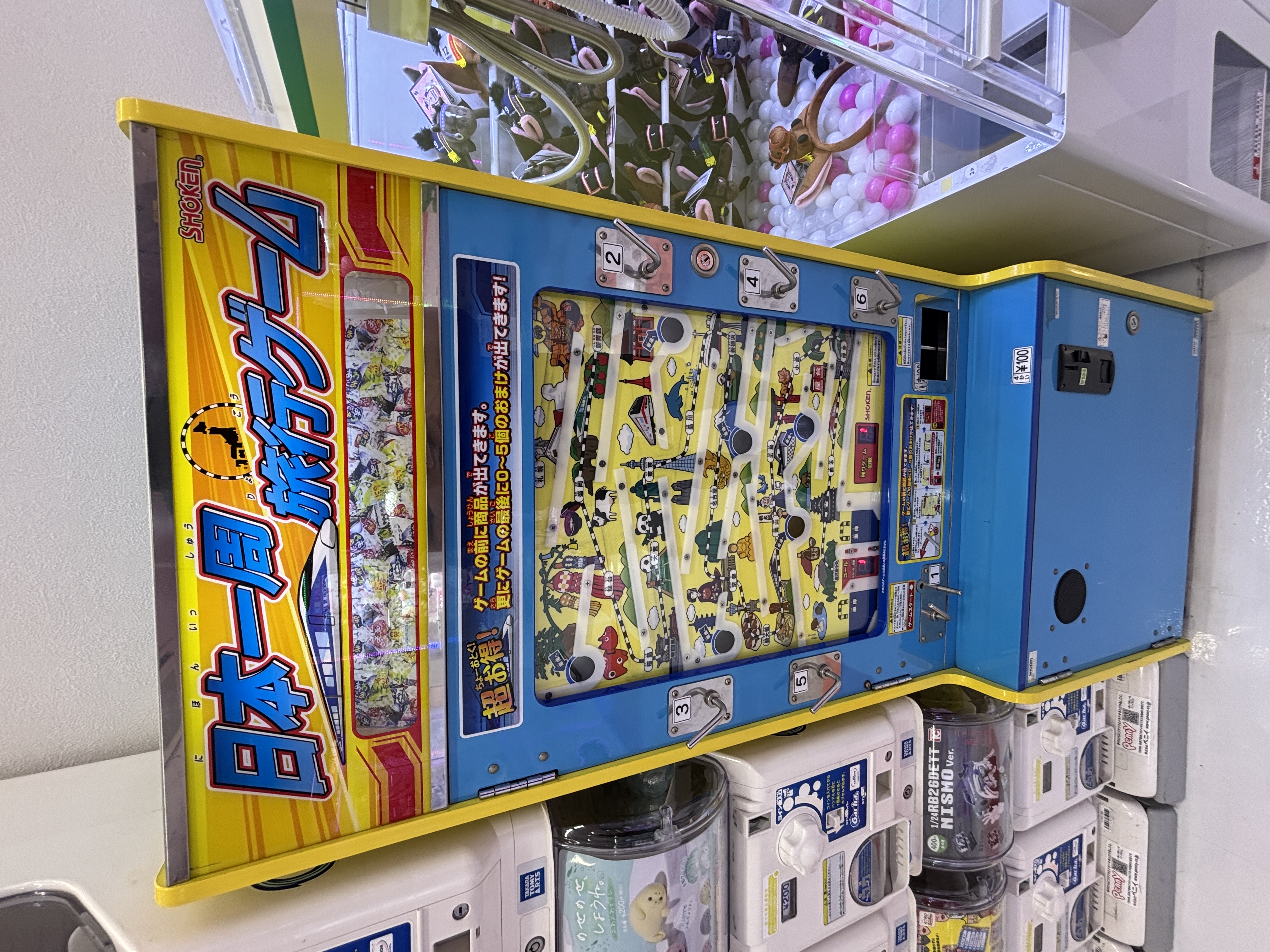 A colourful Japanese vending machine featuring a travel-themed game, displaying various icons and characters related to travel.